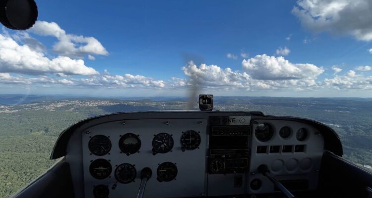 Vista de cockpit de Cessna do Aeroclube de Canela em voo sobre a Serra Gaúcha, horizonte com cidades e nuvens