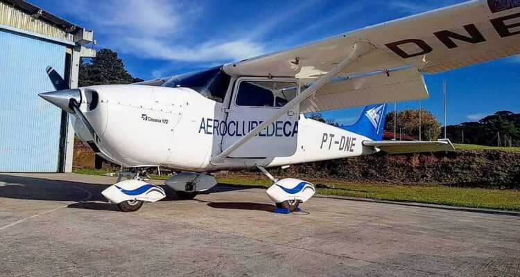 Cessna 172 PT-DNE do Aeroclube de Canela estacionado em frente ao hangar em dia ensolarado