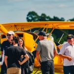 Festejos do 73º aniversário do Aeroclube de Canela no pátio do aeroclube com pessoas se divertindo, aviões chegando e saindo